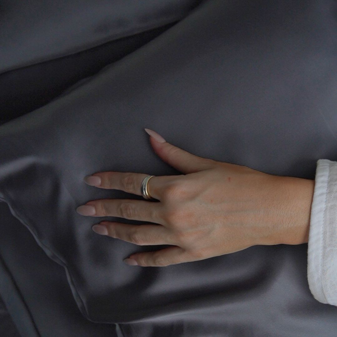 Hand resting on charcoal plant-based silk pillowcase for skin-friendly sleep