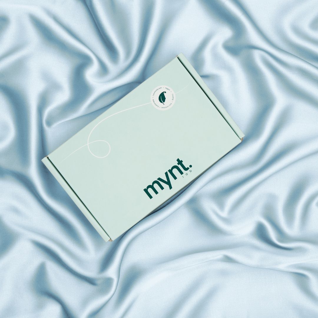 Mynt Lab mint green box on light blue vegan silk bedding, highlighting luxury packaging and sustainable fabric texture