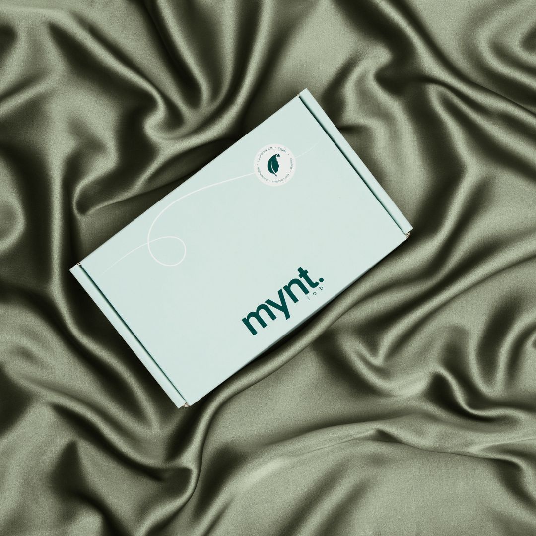 Mynt Lab mint green packaging box on olive green vegan silk bedding background, styled in natural light folds