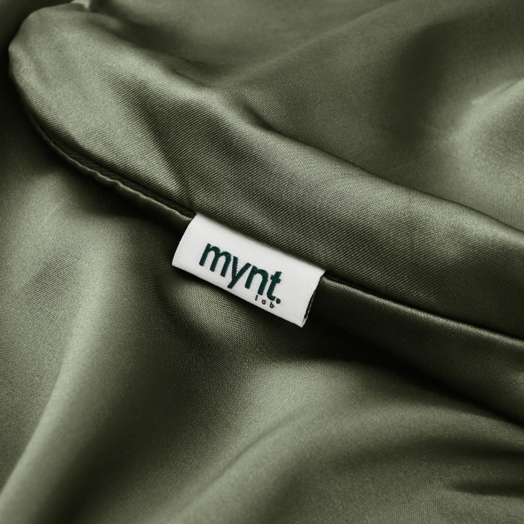 Close-up of olive green vegan silk pillowcase featuring the Mynt Lab label, highlighting the smooth plant-based fabric texture