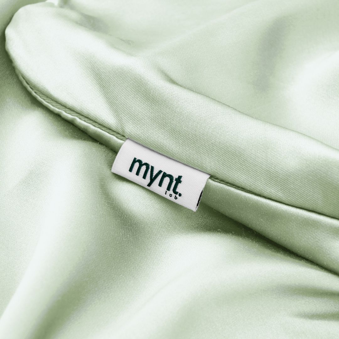 Close-up of sage green vegan silk pillowcase showing Mynt Lab label and buttery-soft plant-based fabric with subtle sheen