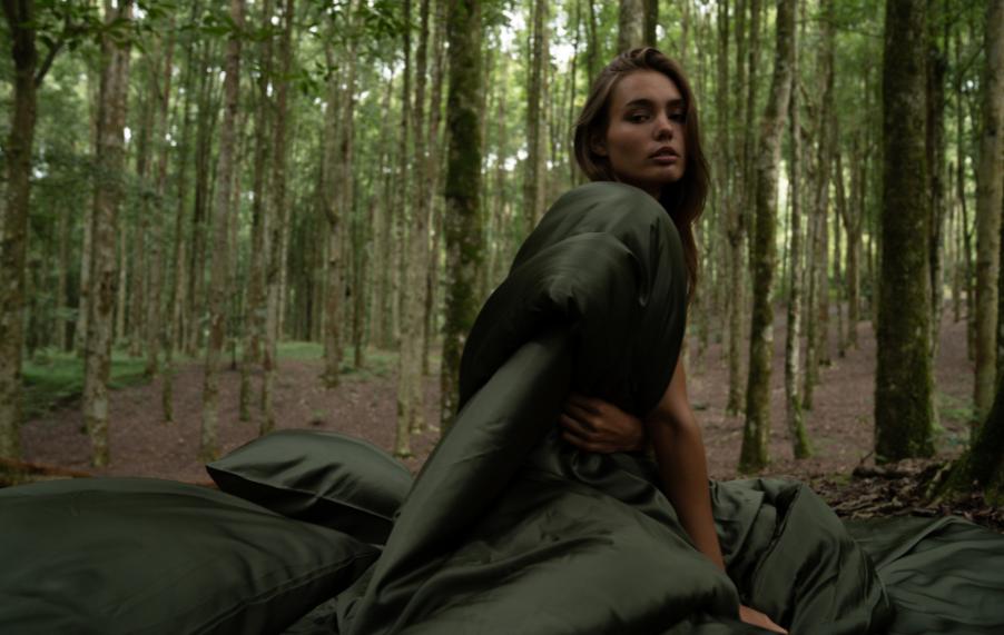 Woman in sustainable forest setting with olive green MyntFusion™ bedding, representing plant-based fabric sourcing