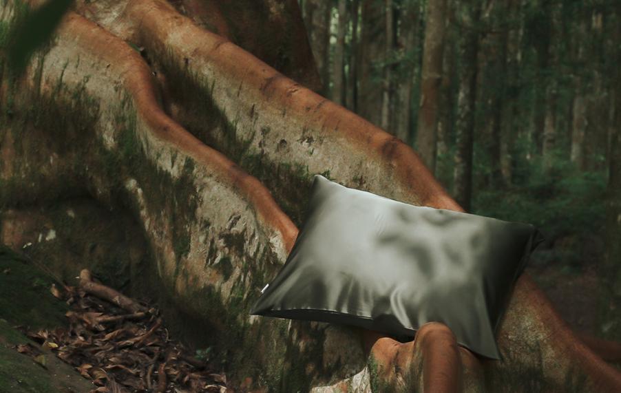 Olive green MyntFusion™ pillowcase on a tree trunk in a forest, representing plant-based bedding materials