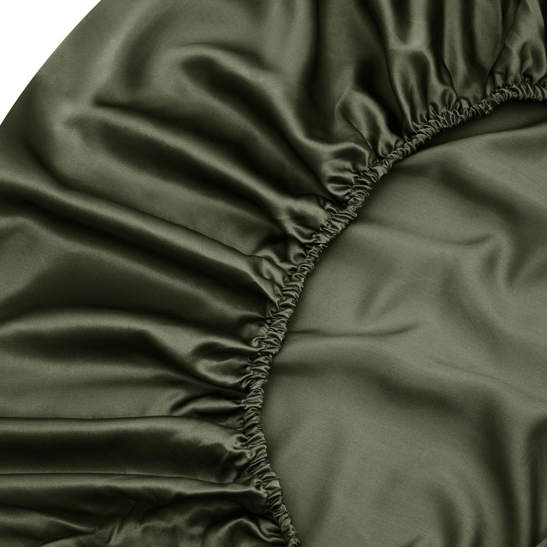 Close-up of the Fitted Sheet Set in olive green, featuring silky soft, smooth, and slightly shiny fabric with gathered elastic edges.