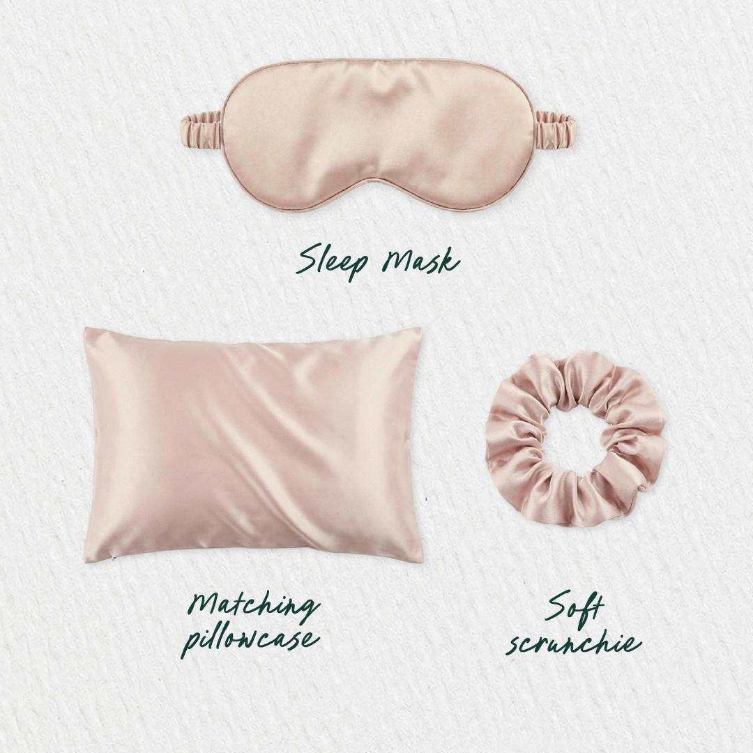 A blush pink satin Beauty Sleep Gift Set—sleep mask, pillowcase, and scrunchie—is displayed on a light textured background with handwritten labels for each: Sleep Mask, Matching Pillowcase, and Soft Scrunchie.