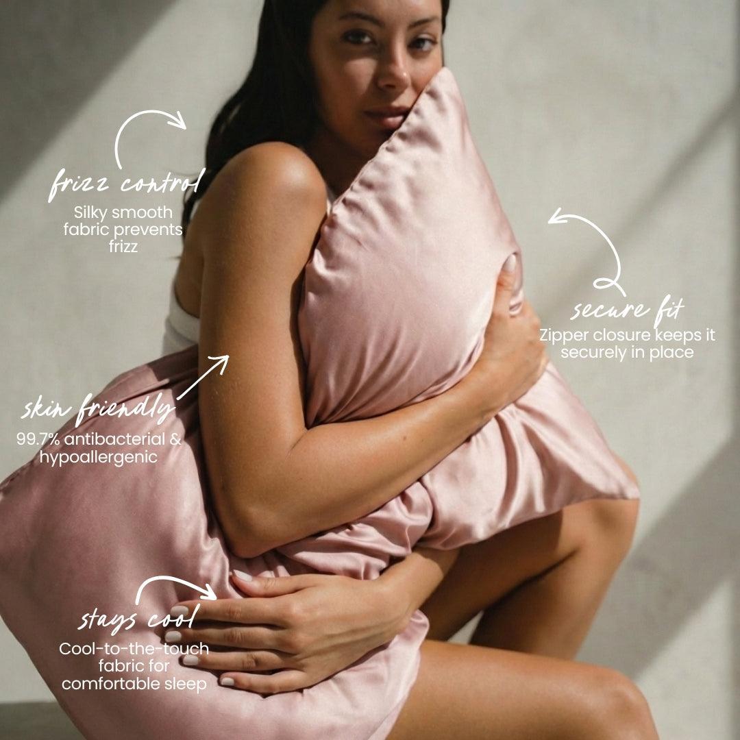 A woman holds a light pink silky pillow from the MyntFusion™ Beauty Sleep Gift Set by Mynt Lab, featuring a cooling, 99.7% antibacterial, hypoallergenic pillowcase with frizz control and a secure zipper for better sleep.
