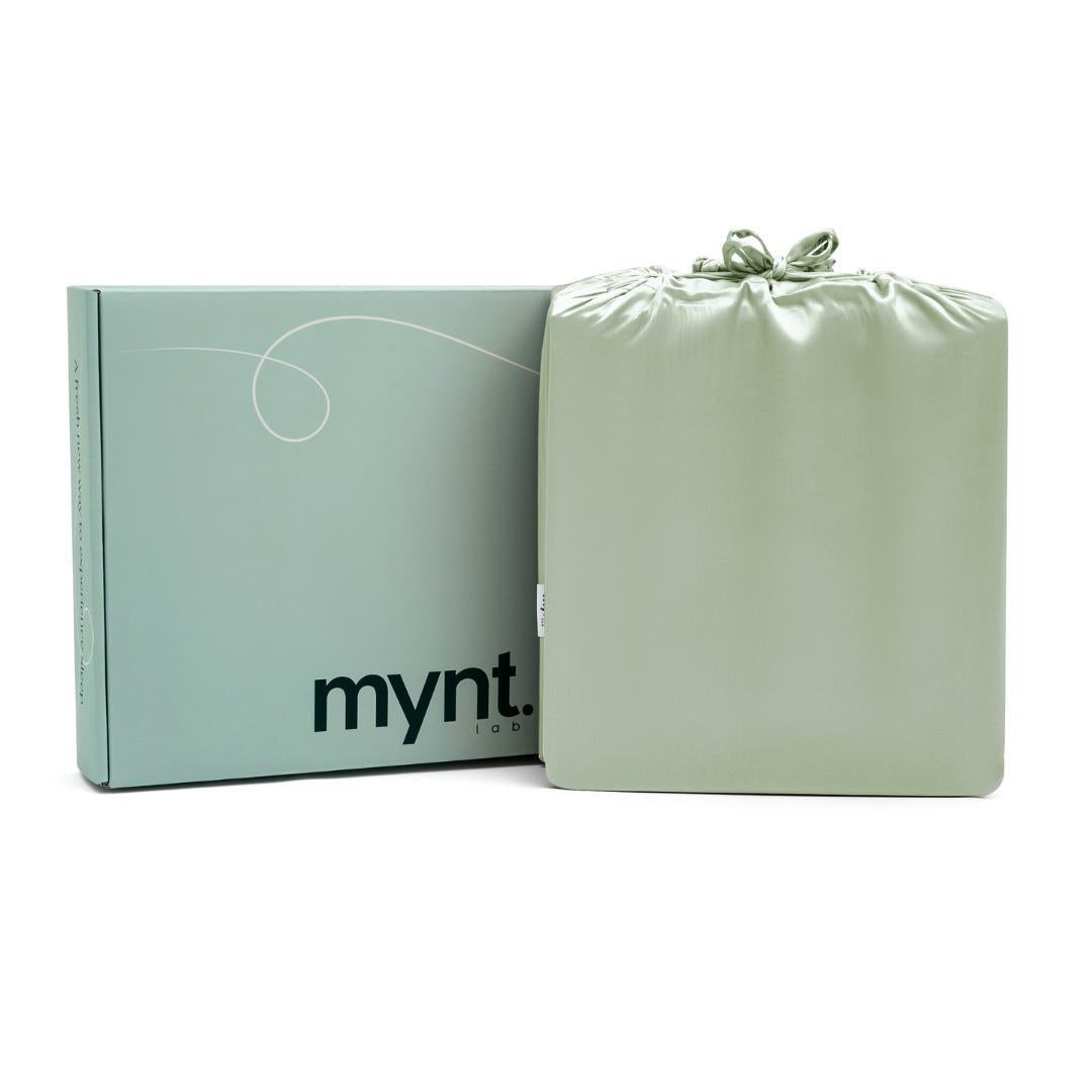 A light green Mynt Lab box stands next to a matching drawstring bag, both sleek and minimalist—ideal for gifting the MyntFusion™ Complete Sheet Set (4-Piece) to elevate any bedroom.