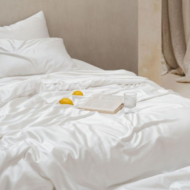 The Mynt Lab MyntFusion™ Complete Bedding Bundle (5-Piece) is shown with white, cooling sheets and pillows, three lemons, an open book, and a glass of water on the cozy bed, set against neutral walls and curtains.