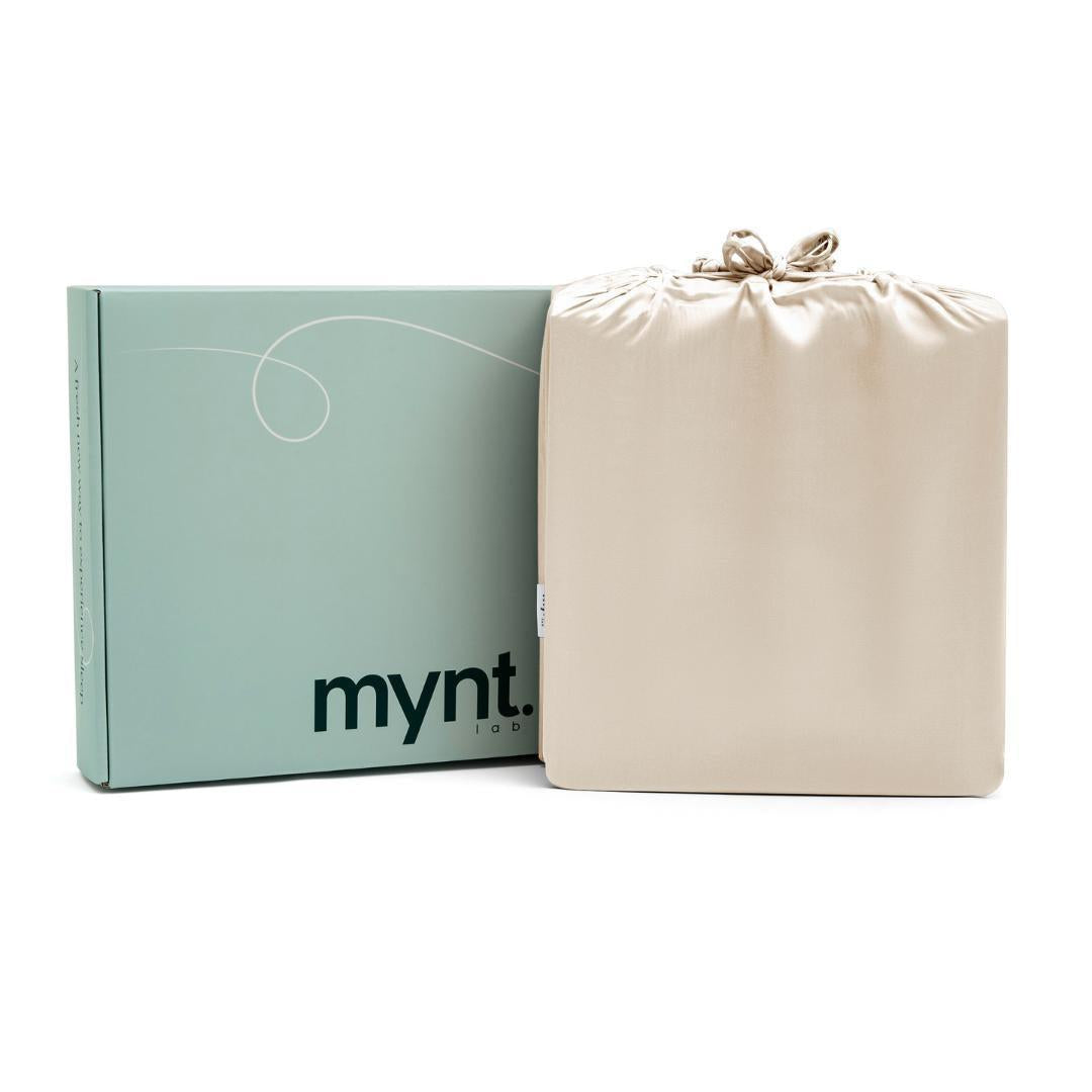 A pale green mynt lab box stands beside a sand silky drawstring bag against a white background - the perfect presentation for the Fitted Sheet Set (3-Piece).