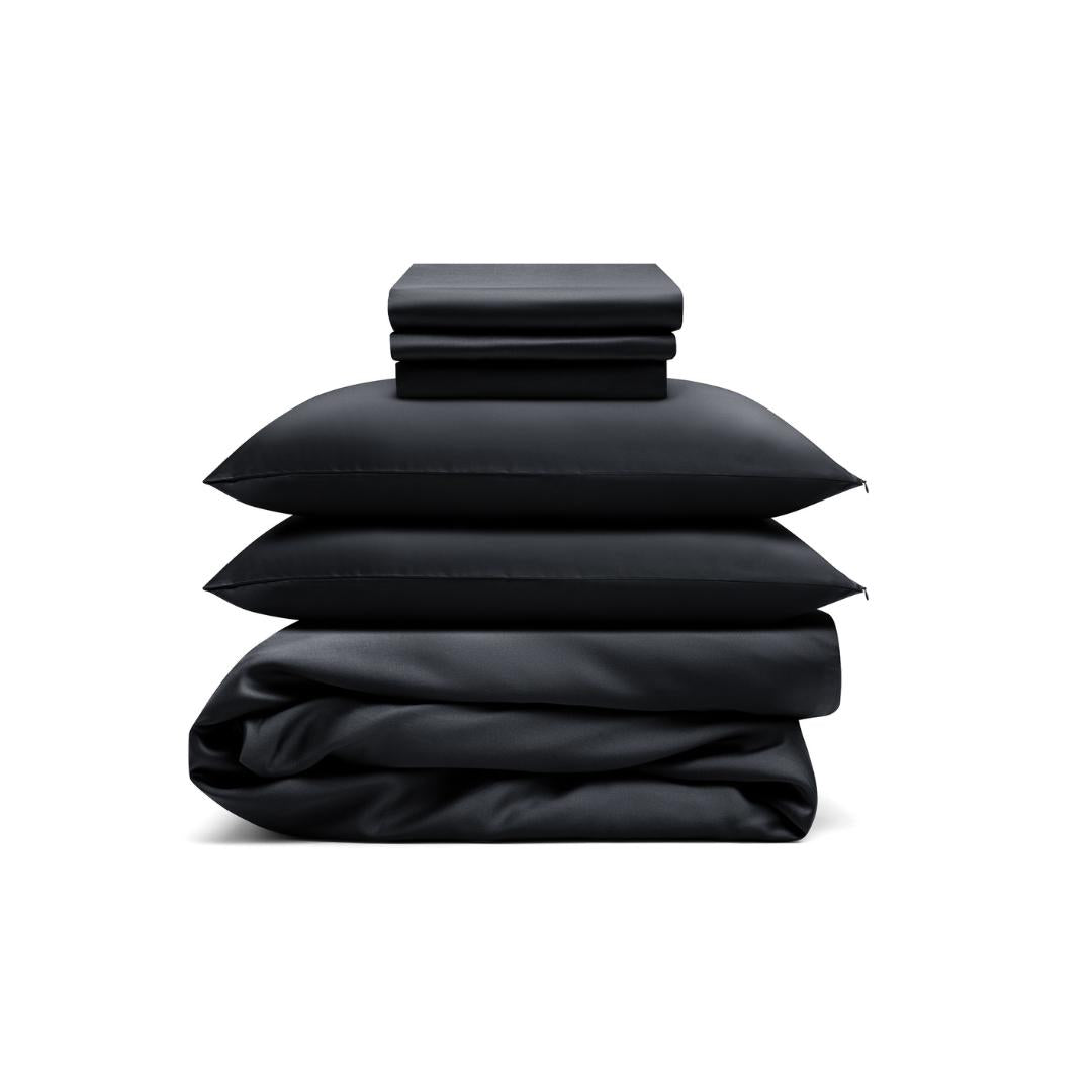 The Bedding Bundle, a customisable set in black, includes folded sheets, two pillows, and a duvet cover, all neatly stacked against a white background.