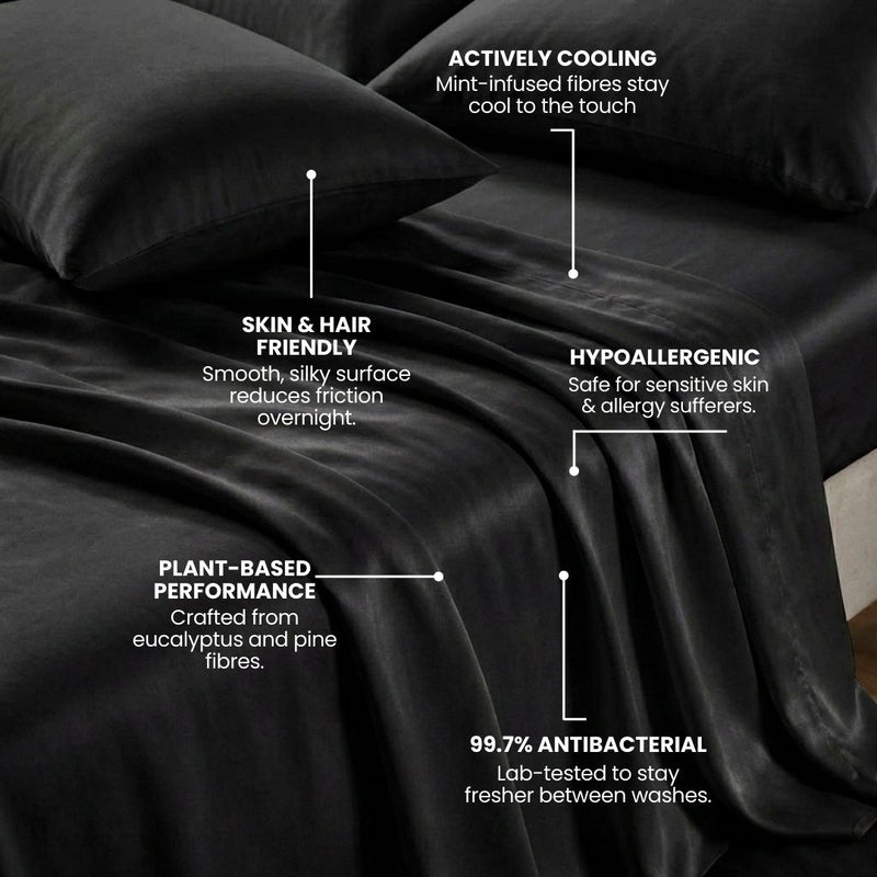 A neatly made bed features the Mynt Lab MyntFusion™ Complete Bedding Bundle (5-Piece) with smooth, shiny black sheets and pillowcases - actively cooling, plant-based, hypoallergenic, skin & hair friendly, and 99.7% antibacterial.
