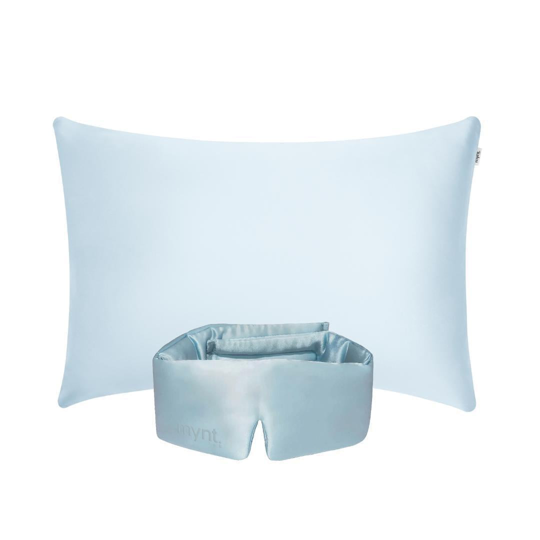 A light blue silk pillowcase and a matching light blue silk sleep mask are arranged against a white background.