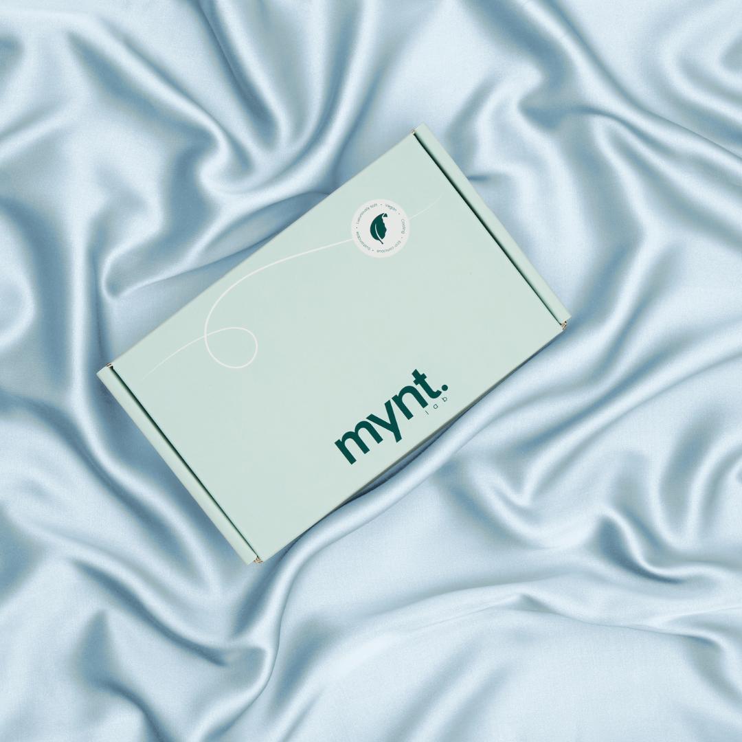 A mint green rectangular box with the brand name mynt lab rests on soft, light blue silky fabric, creating an elegant backdrop - perfect for highlighting the Deep Sleep Bundle for a luxurious and restful night’s sleep.