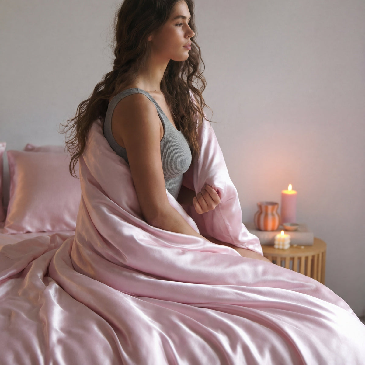 Woman sitting on a bed wrapped in a pink duvet with candles in the background