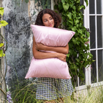 Woman holding pink pillow in an outdoor setting with greenery