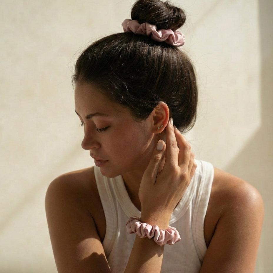 Woman with pink scrunchies in her hair and on her wrist against a neutral background