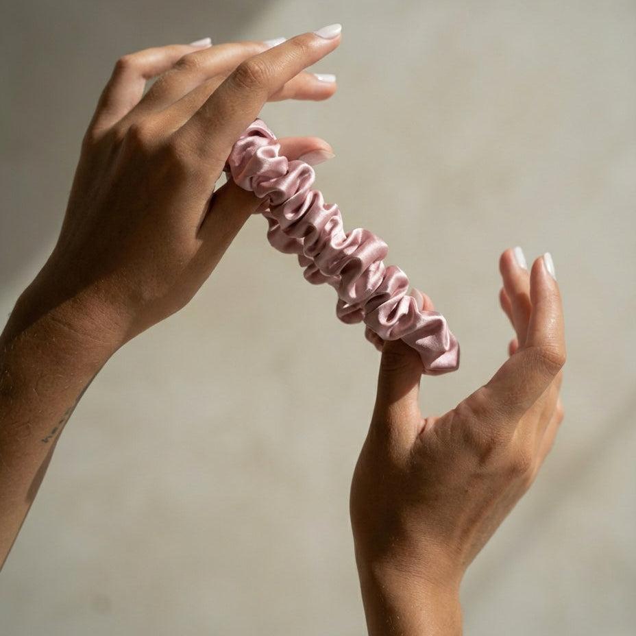 Pink scrunchie held between two hands against a neutral background