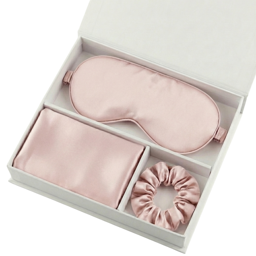 The Beauty Sleep Gift Set comes in a white box with essentials for a perfect night: a light pink silky sleep mask, folded pillowcase, and scrunchie, each neatly arranged in separate compartments.