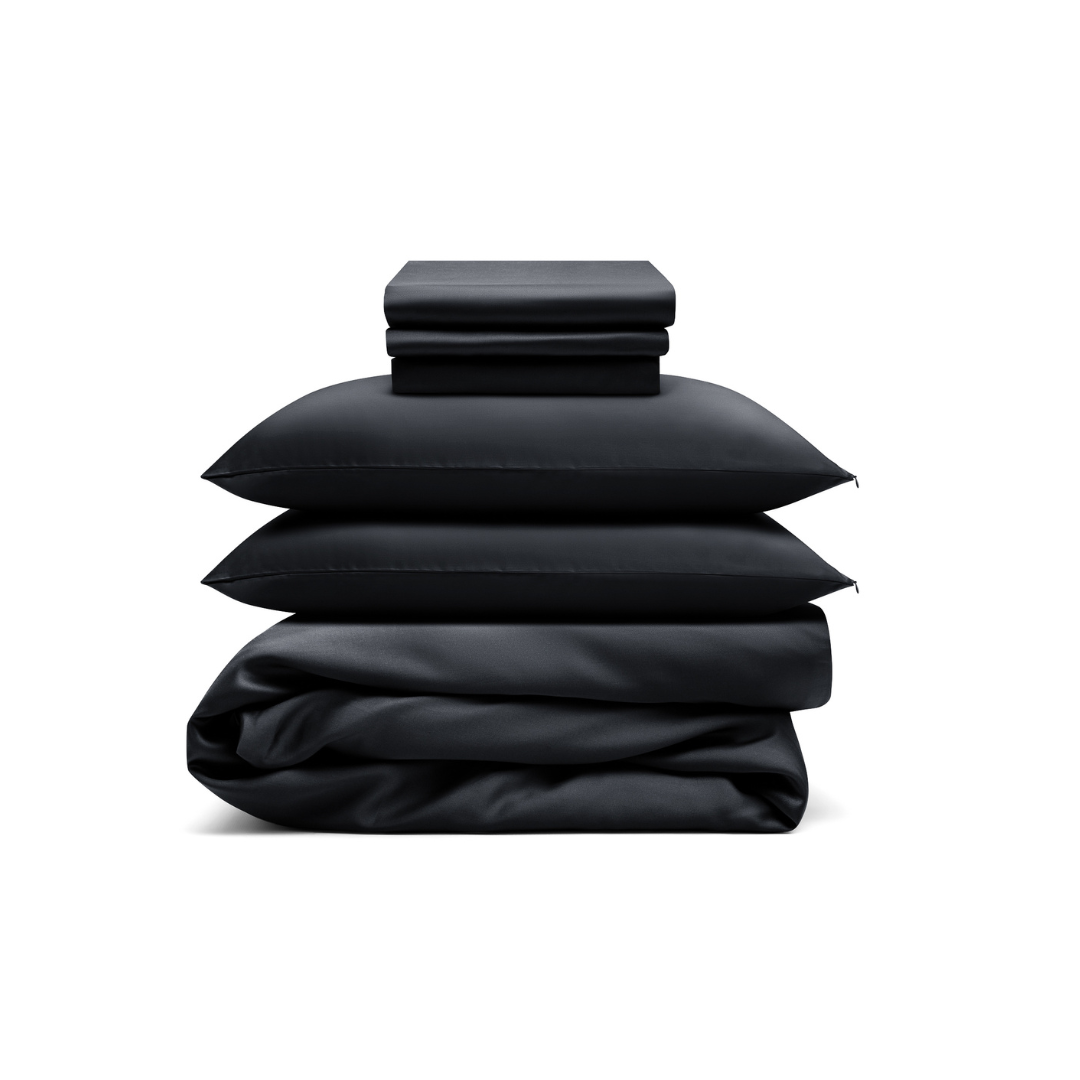 The Bedding Bundle, a customizable set in black, includes folded sheets, two pillows, and a comforter, all neatly stacked against a white background.