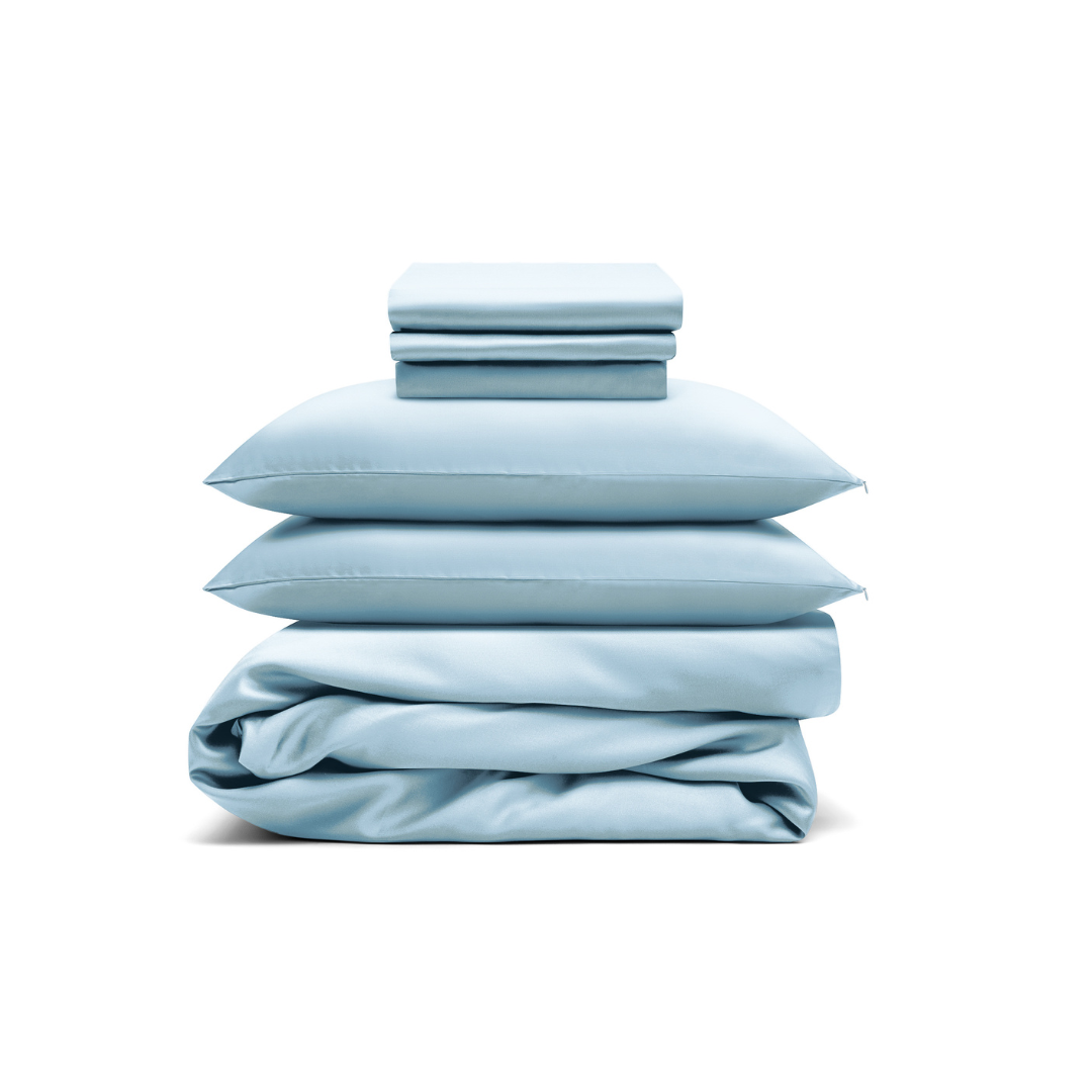 The Bedding Bundle, featuring light blue antibacterial sheets, pillowcases, and a comforter, is neatly stacked and folded against a white background.