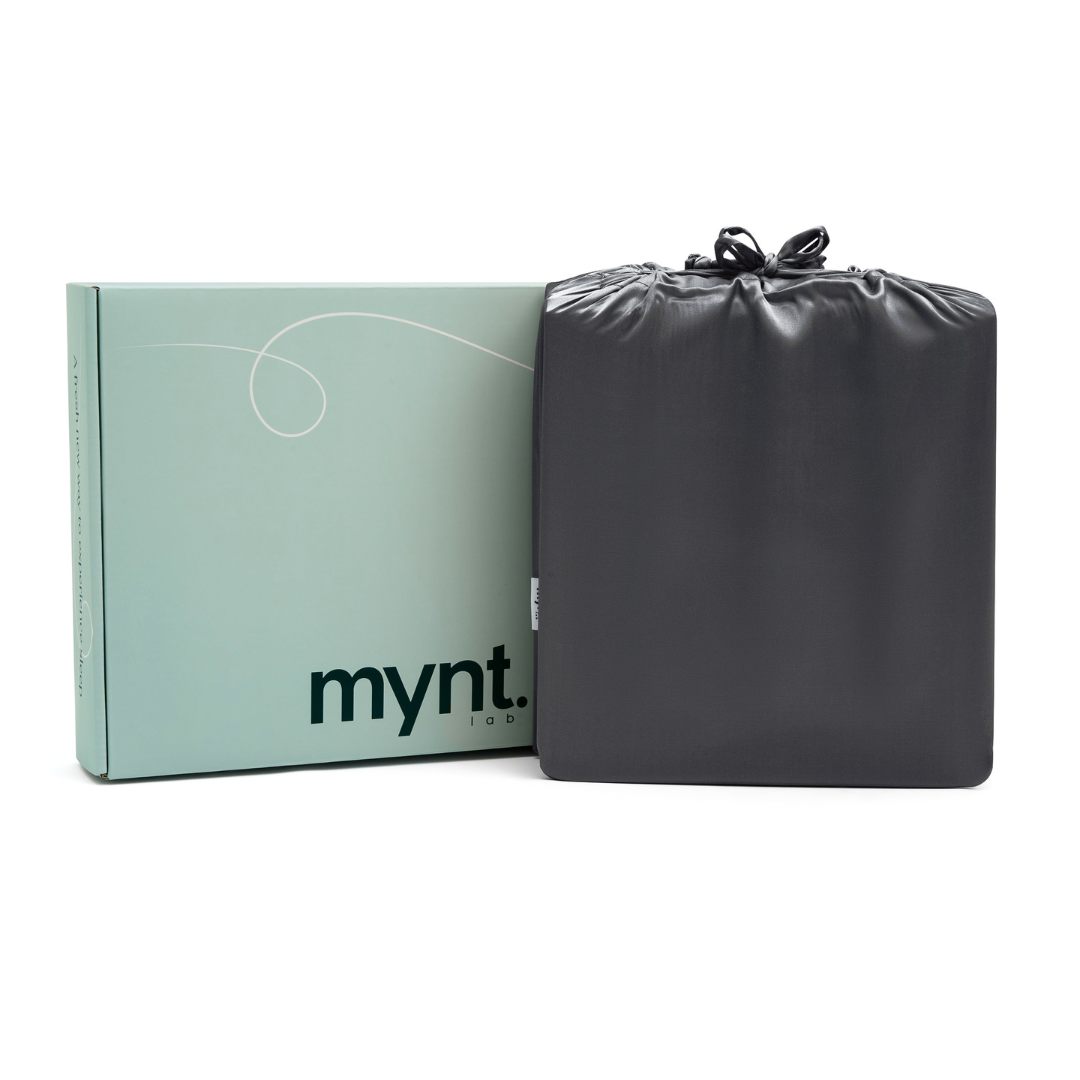 A light green mynt box stands upright beside a neatly folded black drawstring bag against a white background—perfectly showcasing the Fitted Sheet Set (3-Piece).