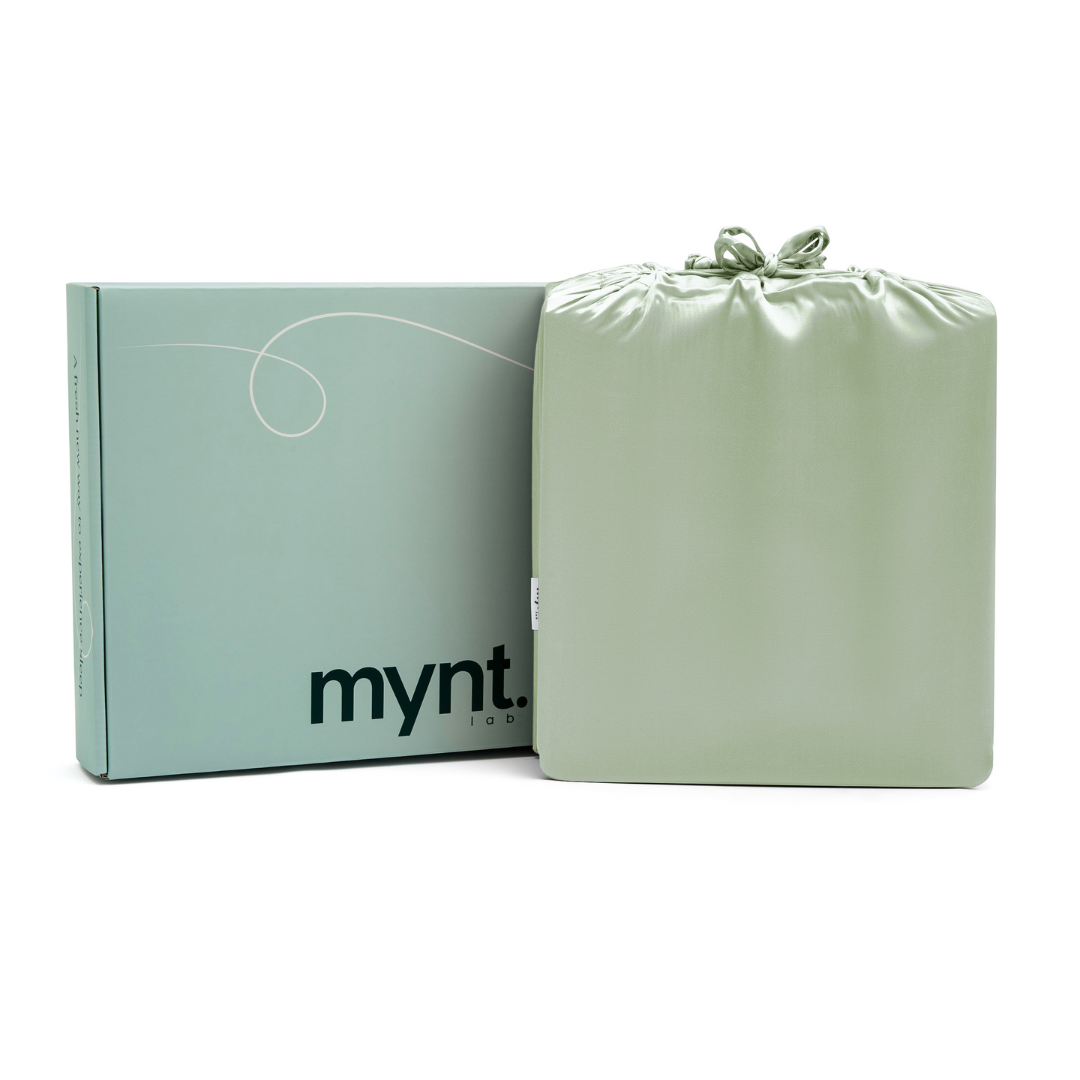A light green drawstring bag rests next to a matching mynt lab-branded box, both hinting at the gentle softness of the Fitted Sheet Set. The items are displayed against a clean white background.