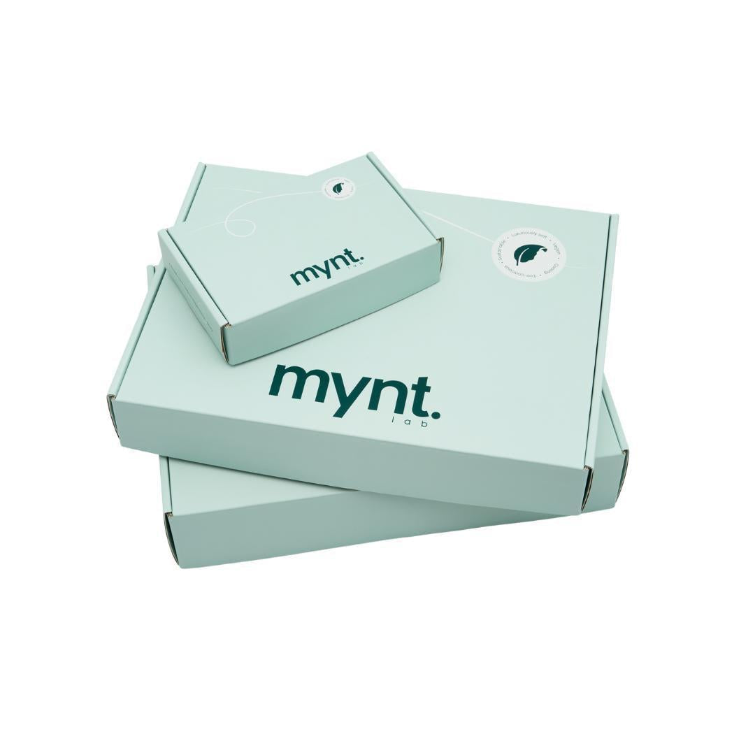 Three mint green cardboard boxes of varying sizes, each labeled "mynt lab" in dark letters and stacked on a white background. The top box features a circular sticker with a stylised leaf logo.