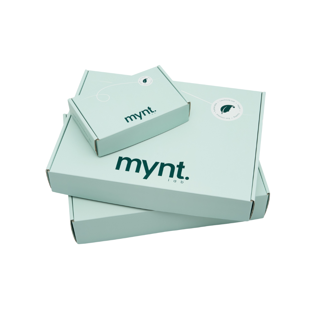 Three mint green cardboard boxes of varying sizes, each labeled "mynt lab" in dark letters and stacked on a white background. The top box features a circular sticker with a stylised leaf logo.