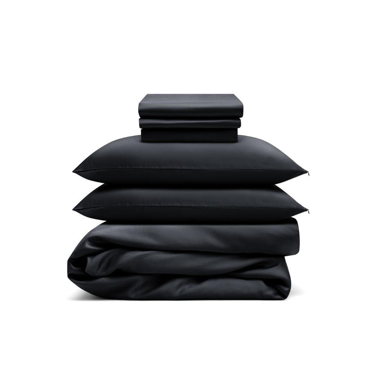 The Bedding Bundle, a customisable set in black, includes folded sheets, two pillows, and a duvet cover, all neatly stacked against a white background.