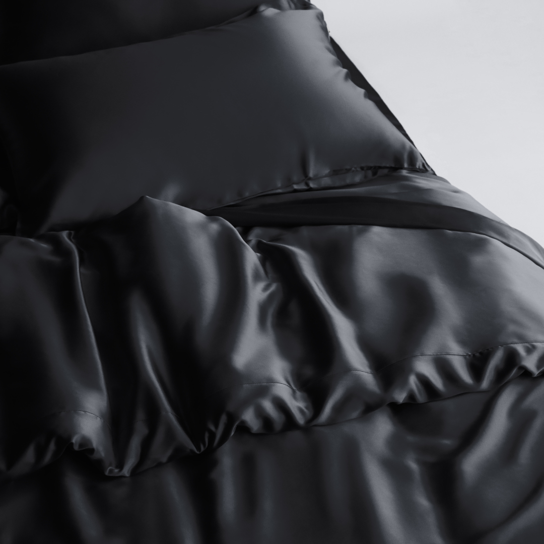 A close-up of a bed featuring smooth, shiny black sheets, a matching pillow, and the Duvet Cover with antibacterial properties for a luxurious, sleek look.