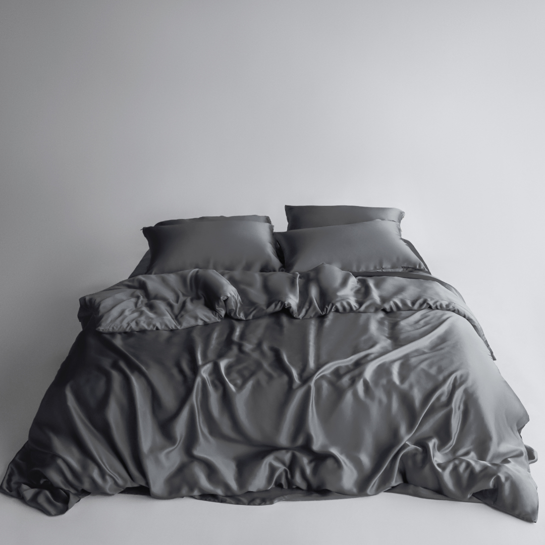 A neatly made bed with two pillows and a dark grey silky duvet cover showcases the Bedding Bundle, customisable to match your unique style and needs, set against a simple light background.