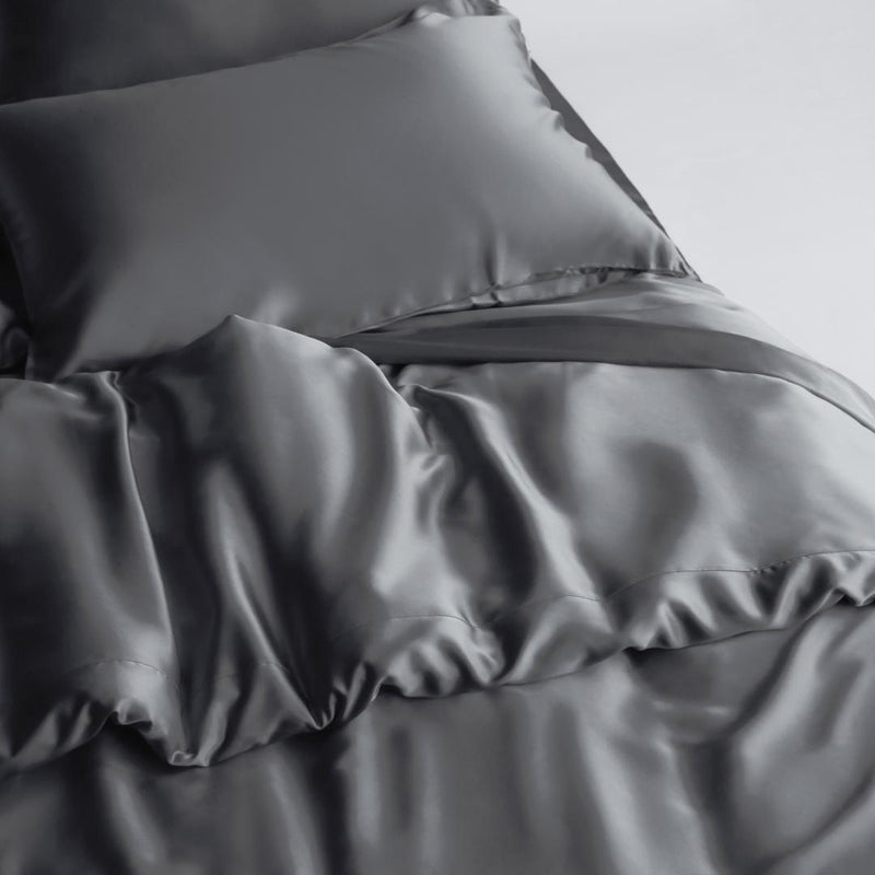 A close-up of a bed shows the Duvet Cover in smooth, shiny charcoal with a matching pillow, highlighting its sustainable materials for a luxurious and elegant look.