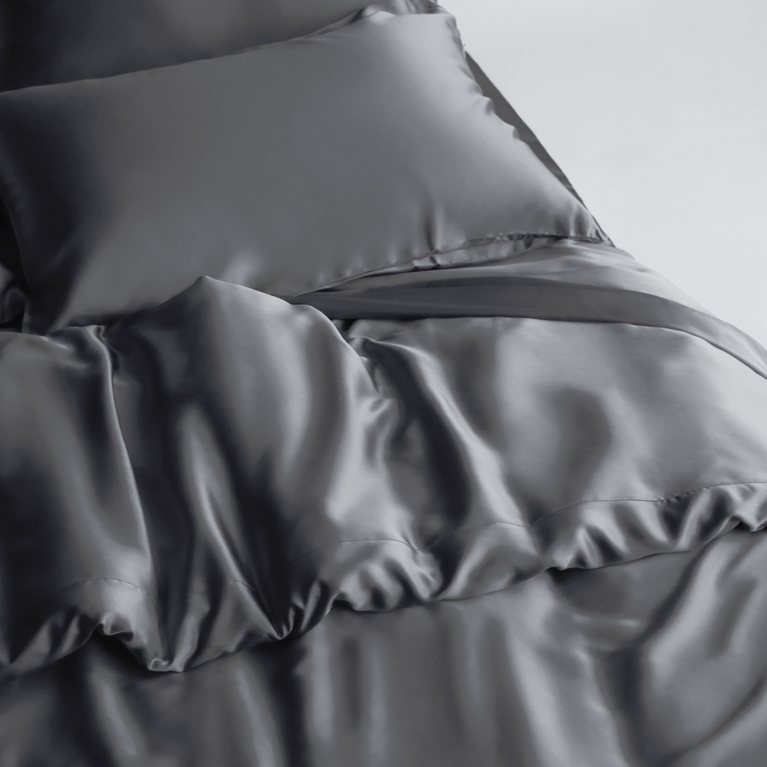 A close-up of a bed shows the Duvet Cover in smooth, shiny dark grey silky fabric with a matching pillow, highlighting its sustainable materials for a luxurious and elegant look.