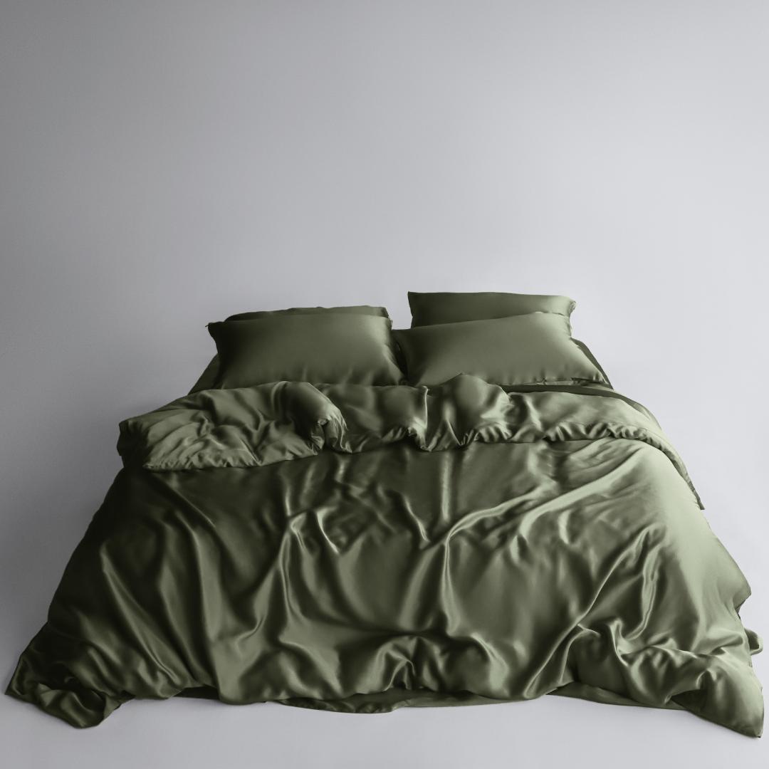A neatly made bed with two pillows and a rumpled olive green duvet cover and sheets from the Bedding Bundle, featuring cooling bedding, set against a plain light grey background.