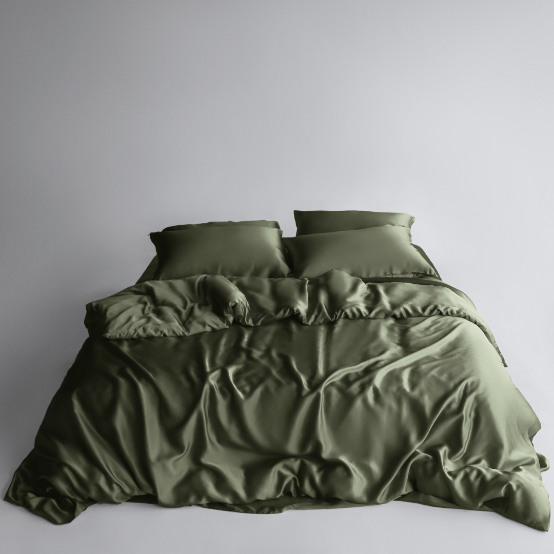 A neatly made bed with two pillows and a rumpled olive green duvet cover and sheets from the Bedding Bundle, featuring cooling bedding, set against a plain light grey background.