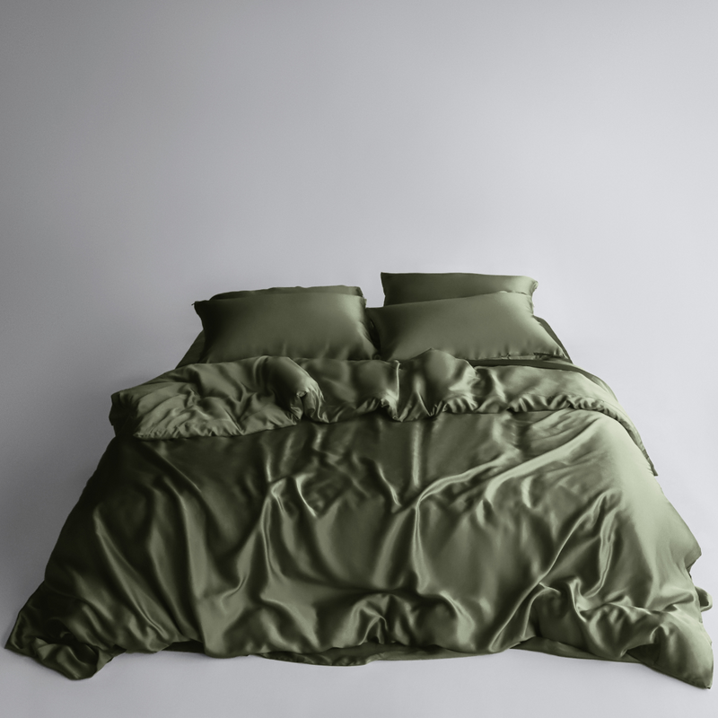 A neatly made bed with two pillows and a rumpled olive green duvet cover and sheets from the Bedding Bundle, featuring cooling bedding, set against a plain light grey background.