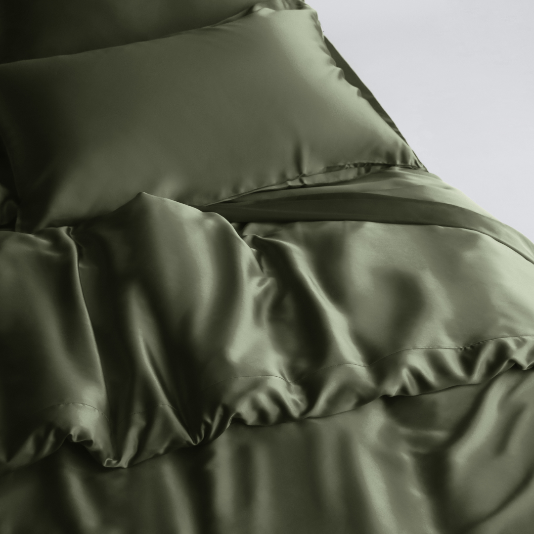 A neatly made bed with shiny, olive green silky Duvet Cover and pillowcases, featuring sustainable bedding for a smooth, luxurious look.