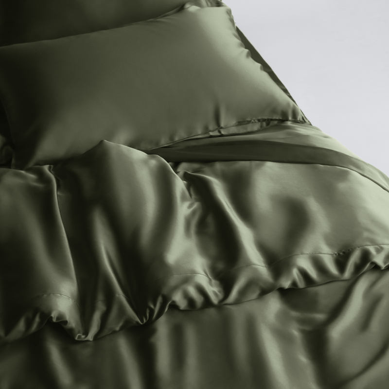 A neatly made bed with shiny, olive green silky Duvet Cover and pillowcases, featuring sustainable bedding for a smooth, luxurious look.