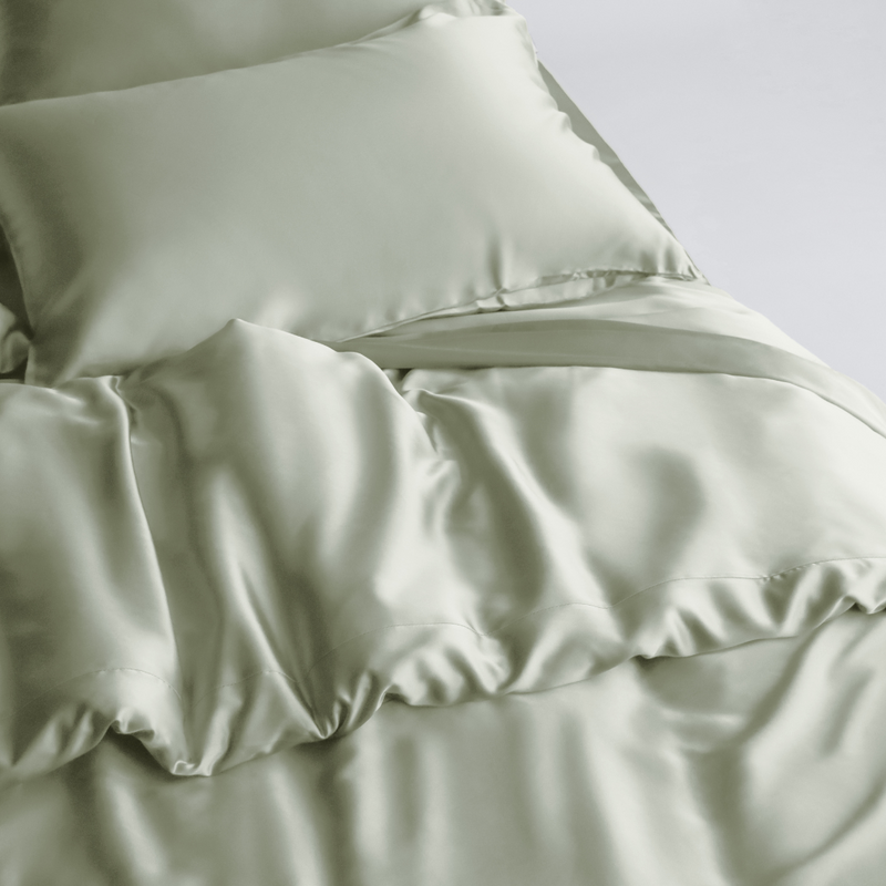 A neatly made bed features a Duvet Cover in soft, light green silky fabric with matching pillowcases. The smooth, shiny fabric and gentle folds create a luxurious look, while sustainable bedding enhances comfort and style for an inviting space.
