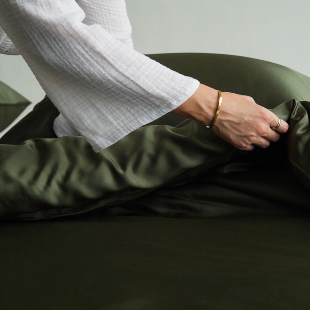 A person in a white long-sleeve shirt and gold bracelet smooths out a olive green-coloured Bedding Bundle.