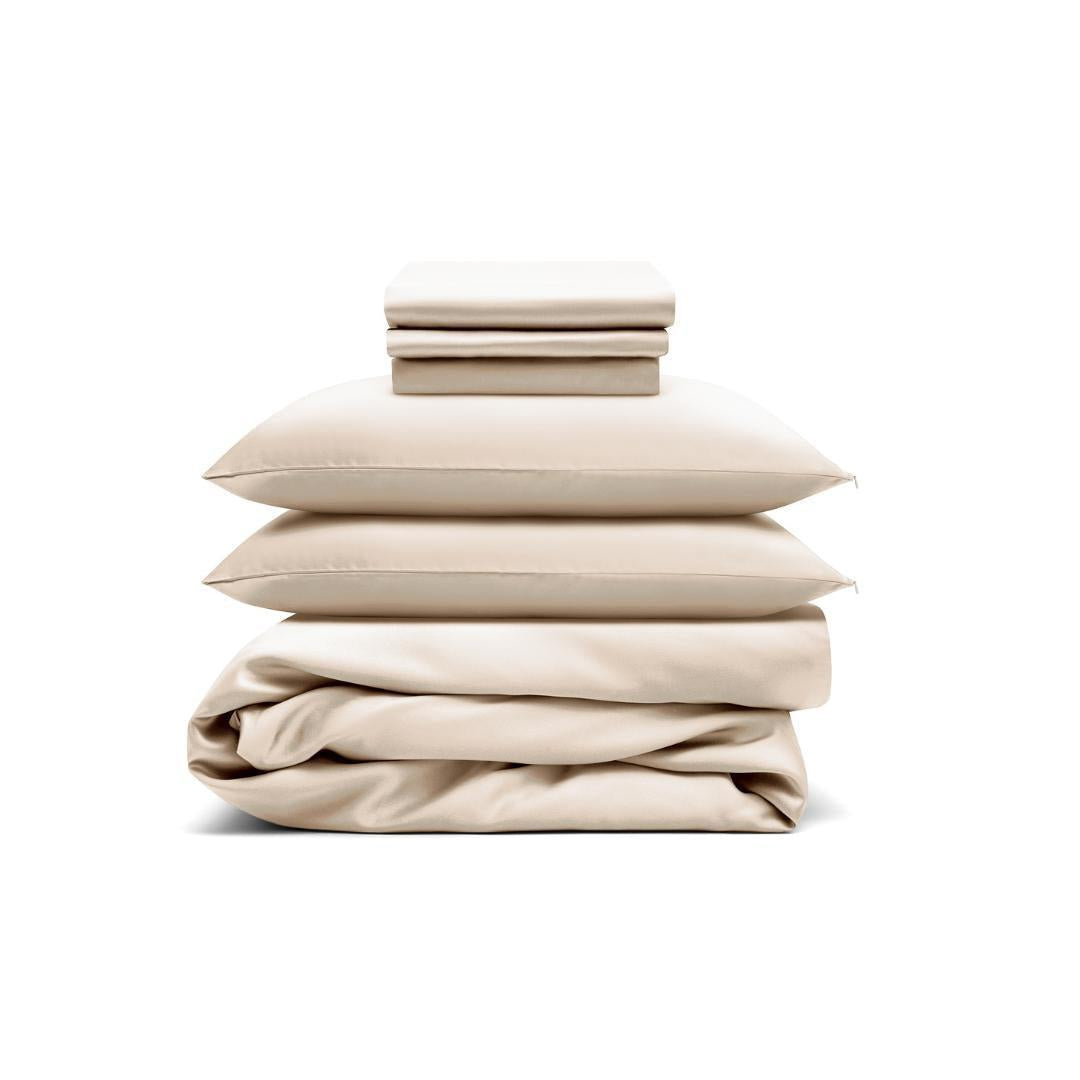 The Bedding Bundle features two folded pillowcases on top, sheet set in the middle, and a folded duvet at the bottom - all sand-coloured and antibacterial - neatly stacked against a white background.