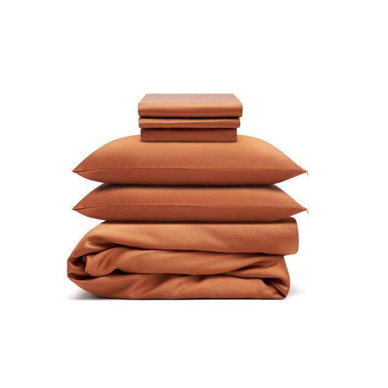 The Bedding Bundle, featuring terracotta-coloured antibacterial sheets, pillowcases, two pillows, and a duvet cover, is neatly stacked and folded against a plain white background.