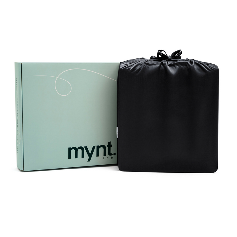 A light teal box labeled "mynt" sits beside a black drawstring bag, both set against a white background—suggesting the premium comfort of the Black Fitted Sheet Set inside.