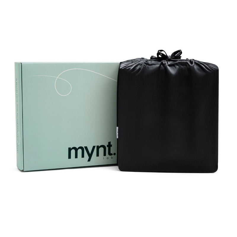 A mint green box labeled "mynt lab" sits beside a black drawstring bag, both set against a white background - suggesting the premium comfort of the Black Fitted Sheet Set inside.