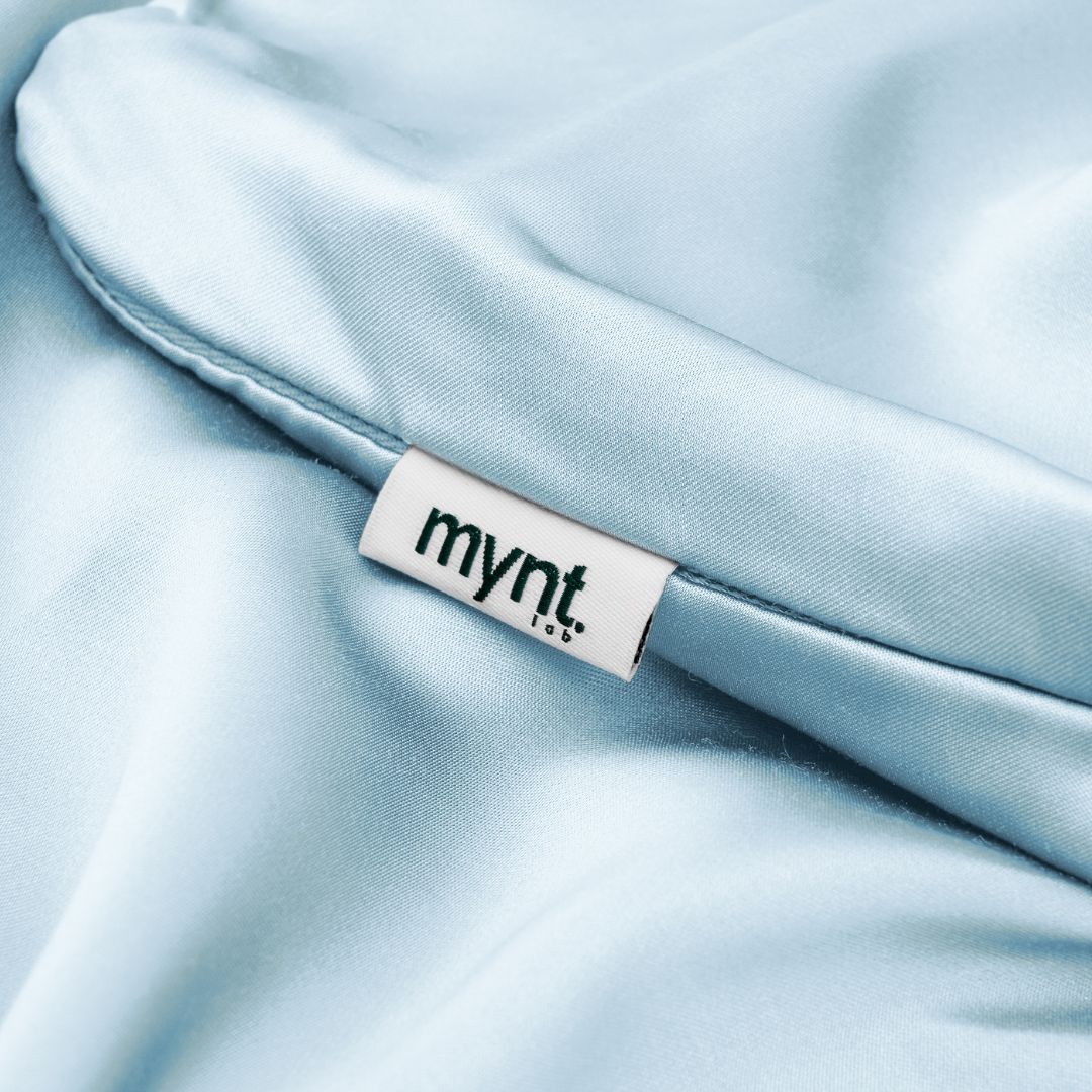 Close-up of light blue vegan silk pillowcase with Mynt Lab label, showcasing soft, sustainable fabric texture