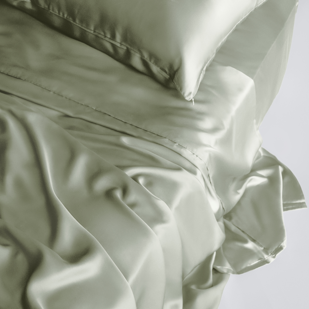 A close-up of the Complete Sheet Set (4-Piece) in sage green, featuring silky soft sheets and a matching pillowcase with a smooth, silky, and luxurious texture highlighted by gentle folds and soft lighting.