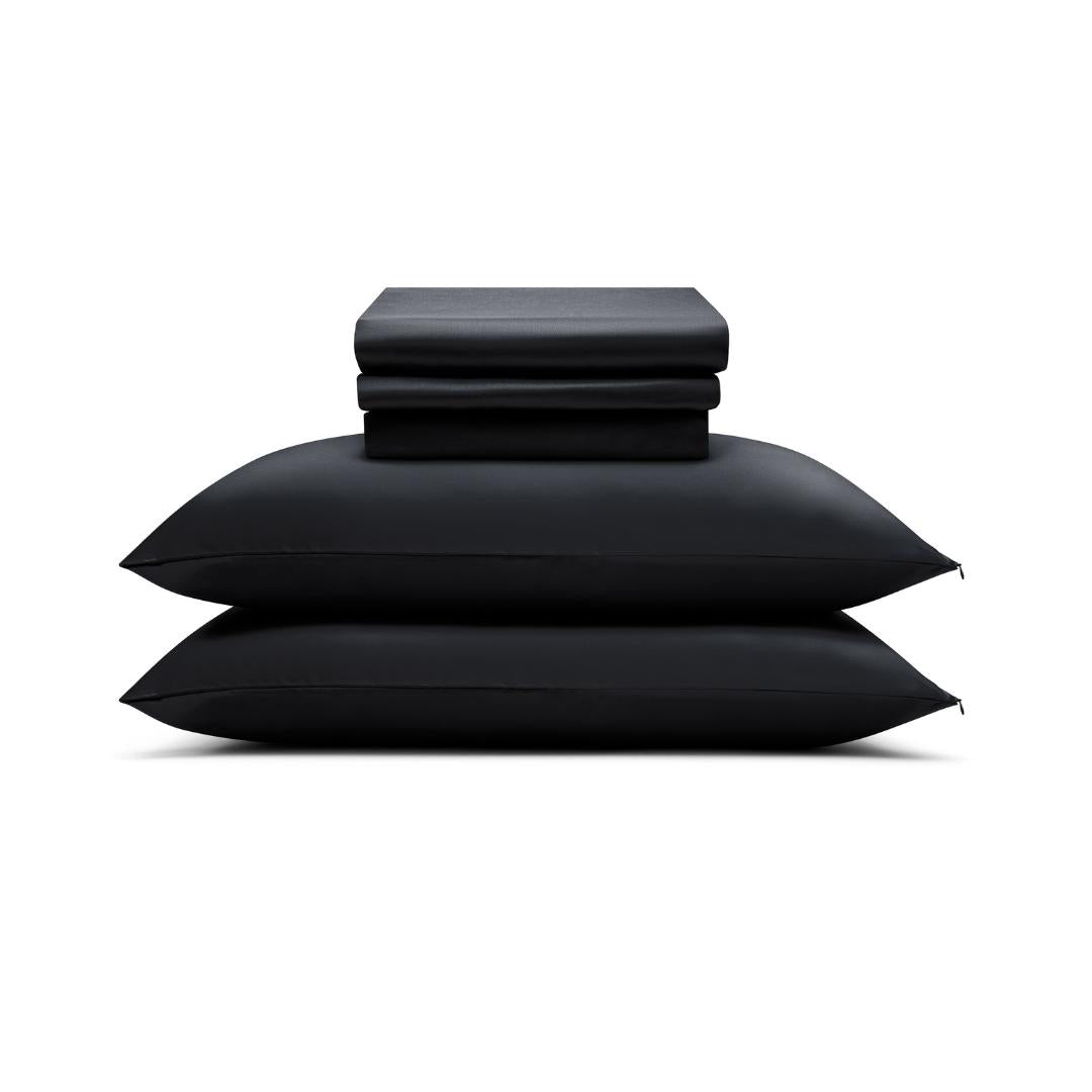 A folded Complete Sheet Set (4-Piece) rests neatly atop two stacked black pillows, all displayed against a white background.