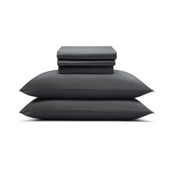 Two neatly stacked charcoal pillows with the Complete Sheet Set (4-Piece) - folded silky soft sheets and pillowcases - arranged on top, all set against a plain white background.