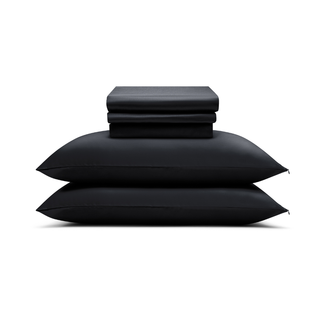 A folded Complete Sheet Set (4-Piece) rests neatly atop two stacked black pillows, all displayed against a white background.