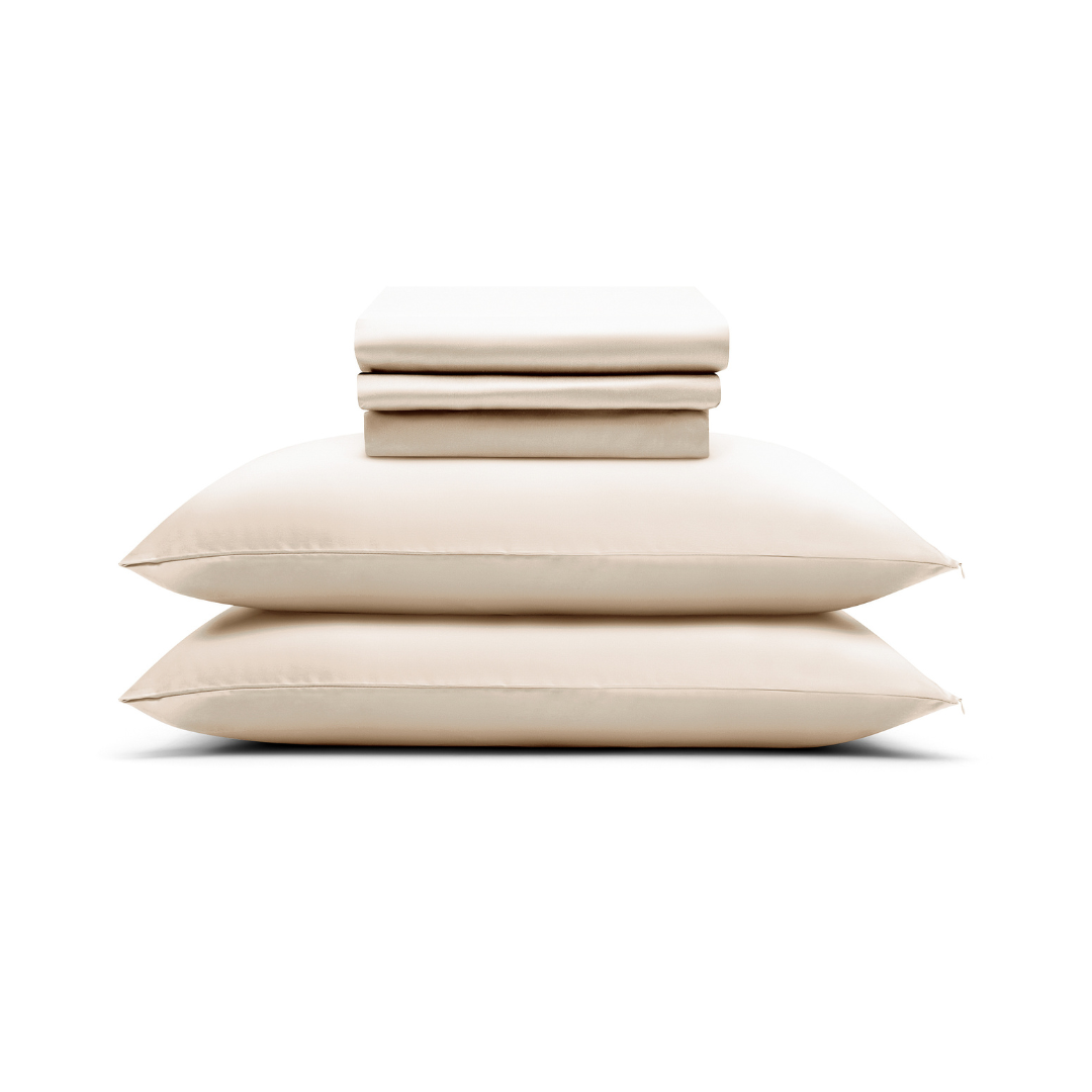 A folded Complete Sheet Set (4-Piece) rests atop two stacked beige pillows, all arranged against a plain white background.